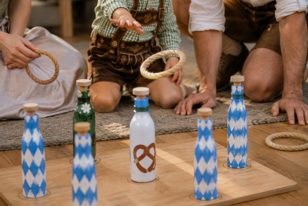 Kind spielt Ringwurf mit bemalten Flaschen bei einer Mini-Wiesn zuhause.
